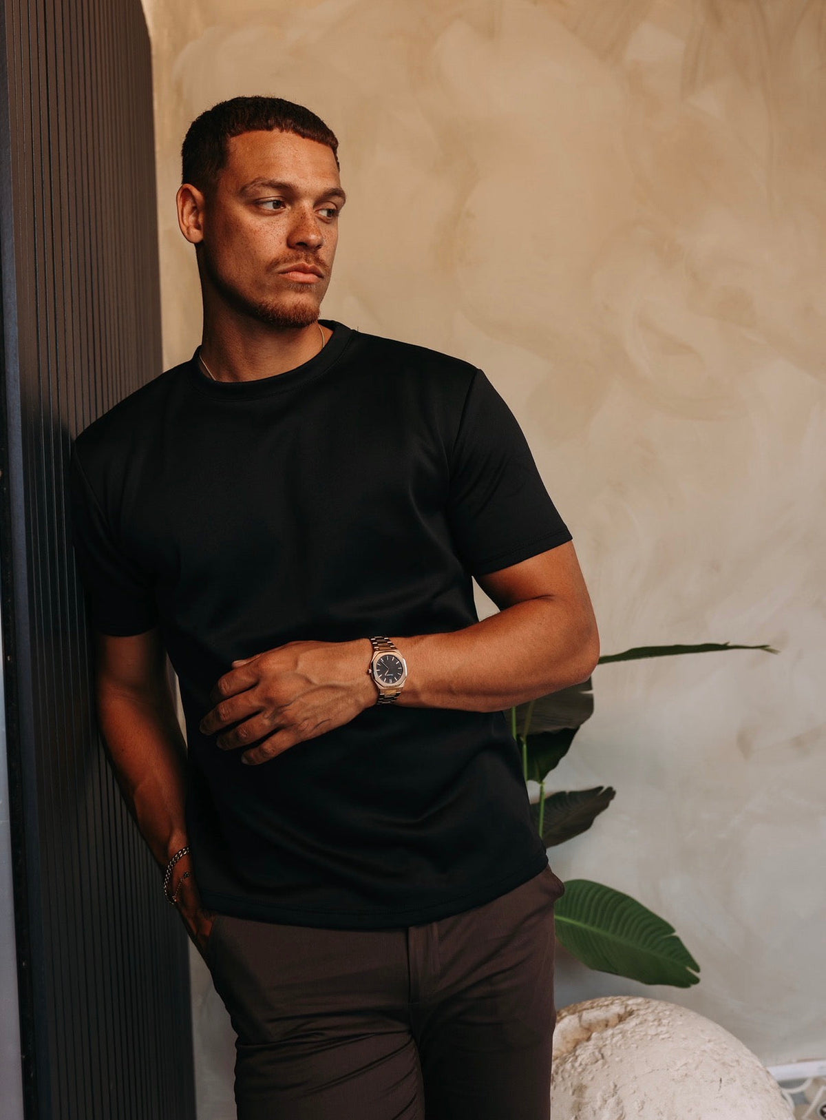 Model in het zwarte Gloss Essential Shirt, leunend tegen een donkere wand