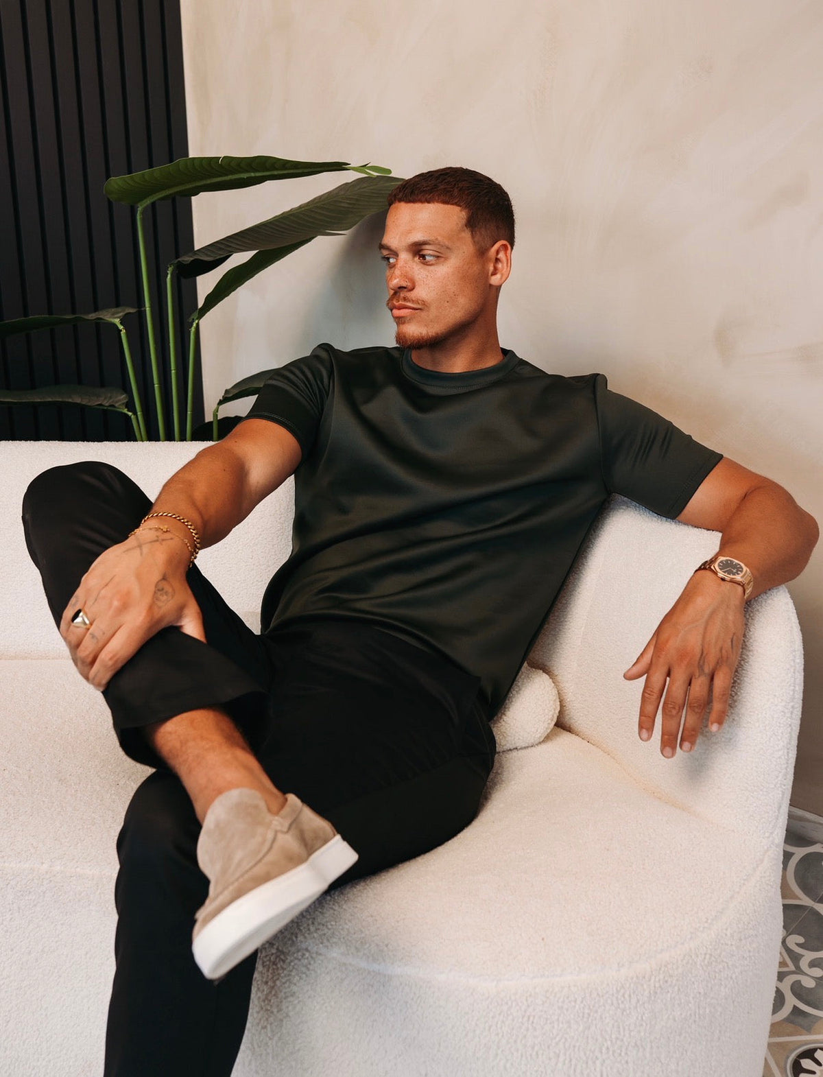 Model zit ontspannen in een witte stoel in het Gloss Essential Shirt in midnight olive