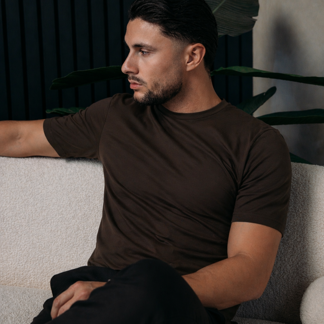 Model in het Shiny Essential Shirt in deep brown, zittend op een witte bank
