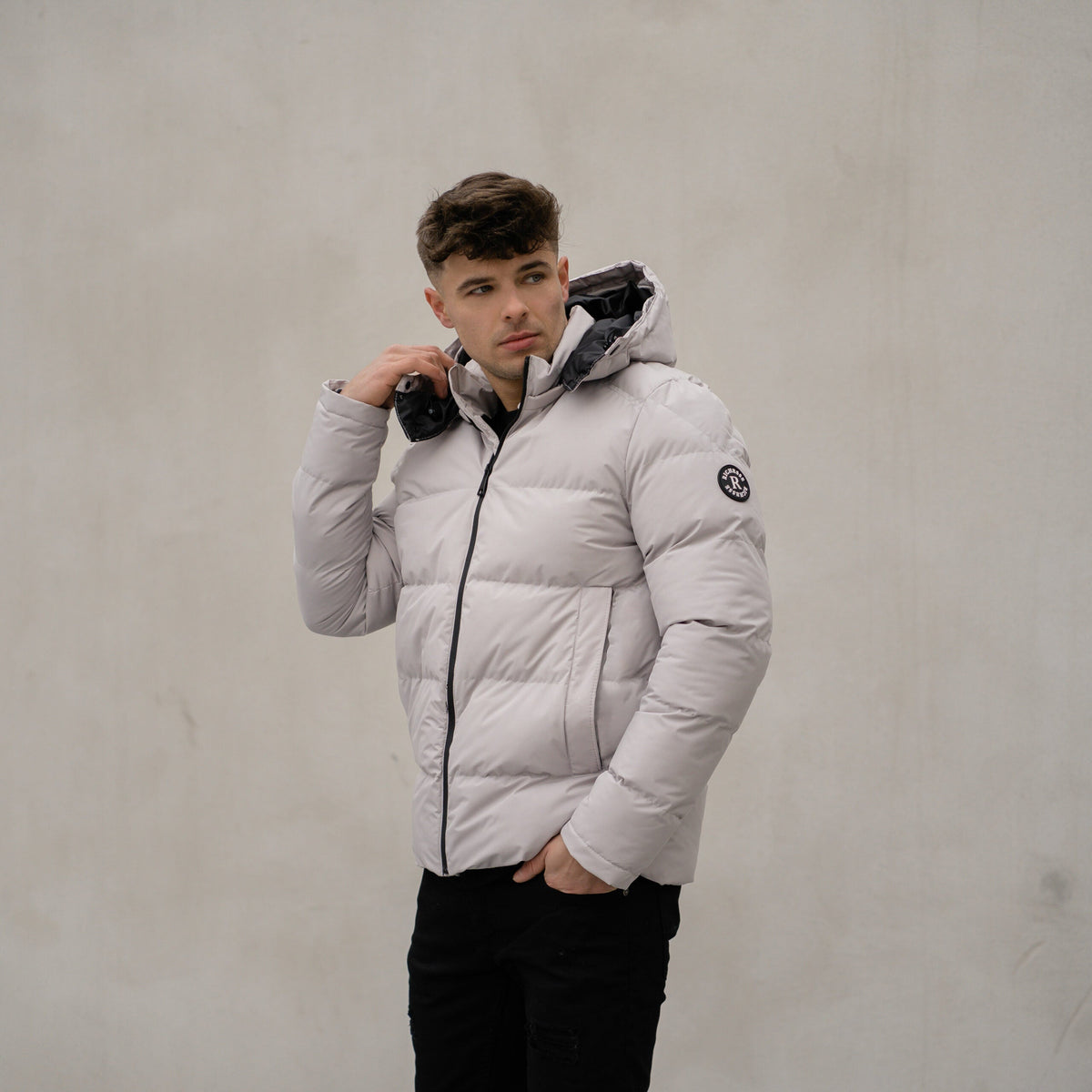 Model in de lichte Devon Puffer Jas met capuchon, tegen een betonnen muur