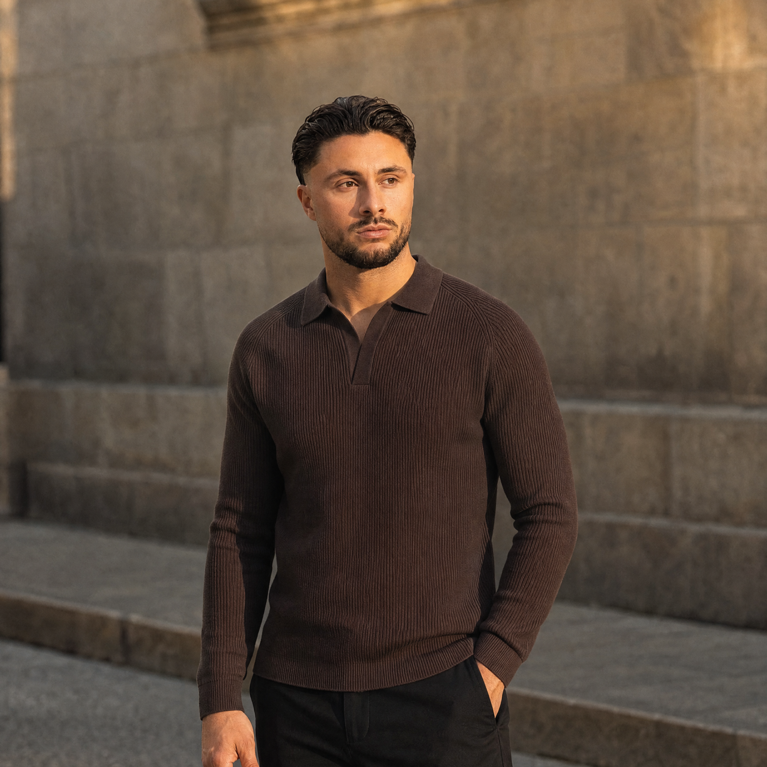 Model in de bruine Ribbed Knit Polo voor een stenen muur