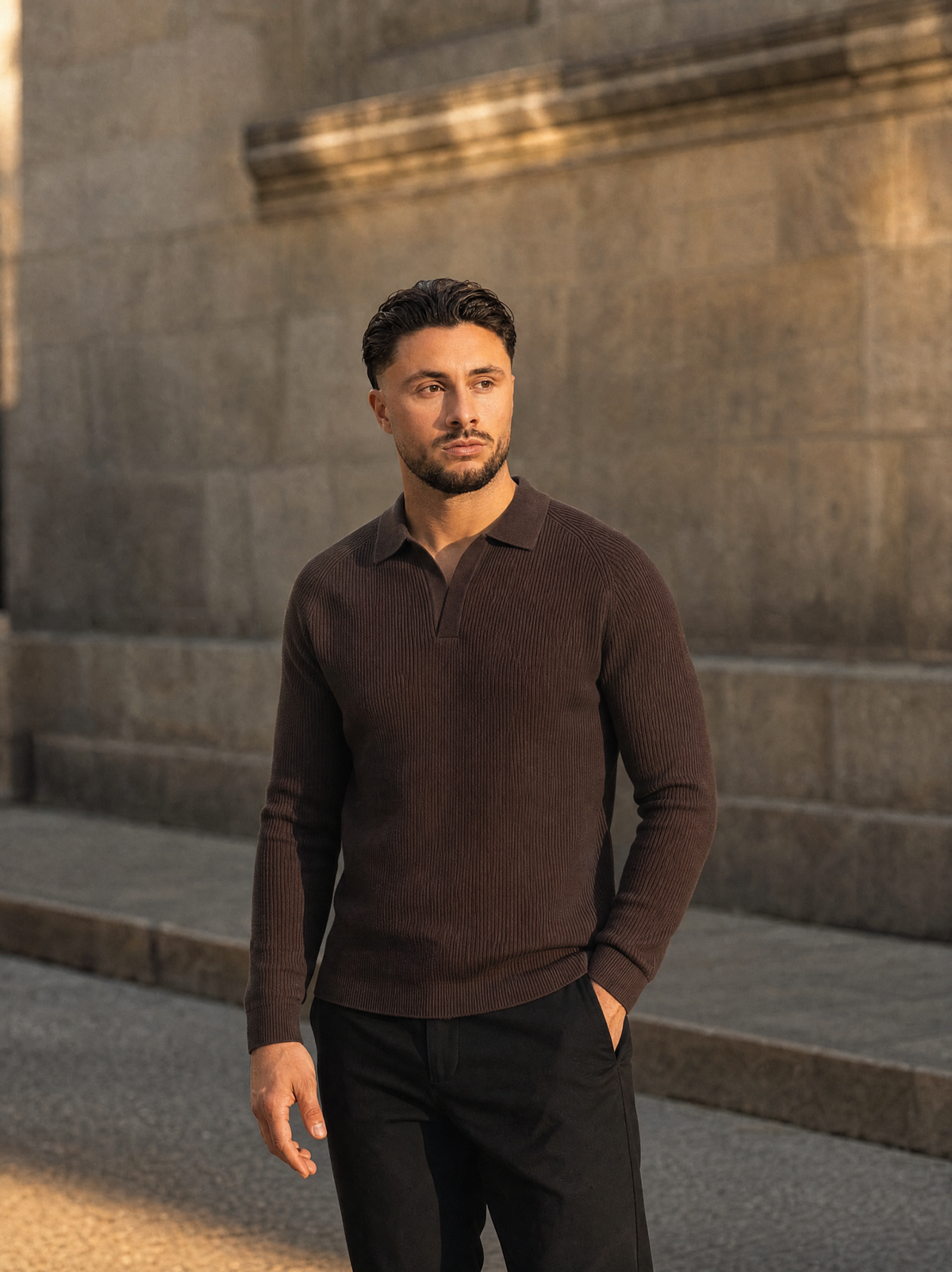 Model in de bruine Ribbed Knit Polo voor een stenen muur
