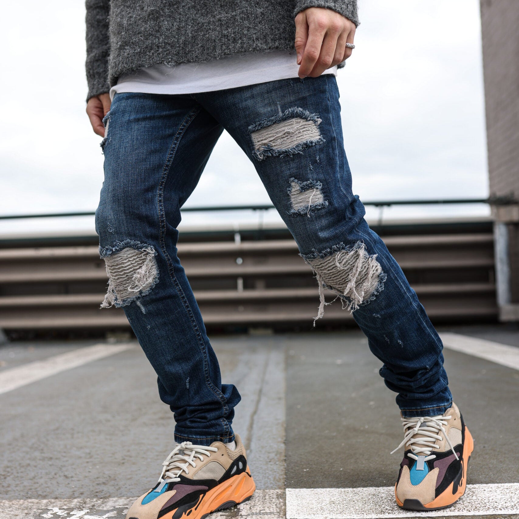 Model in de Force Dark Blue Jeans met scheuren en sneakers op een dak in de stad
