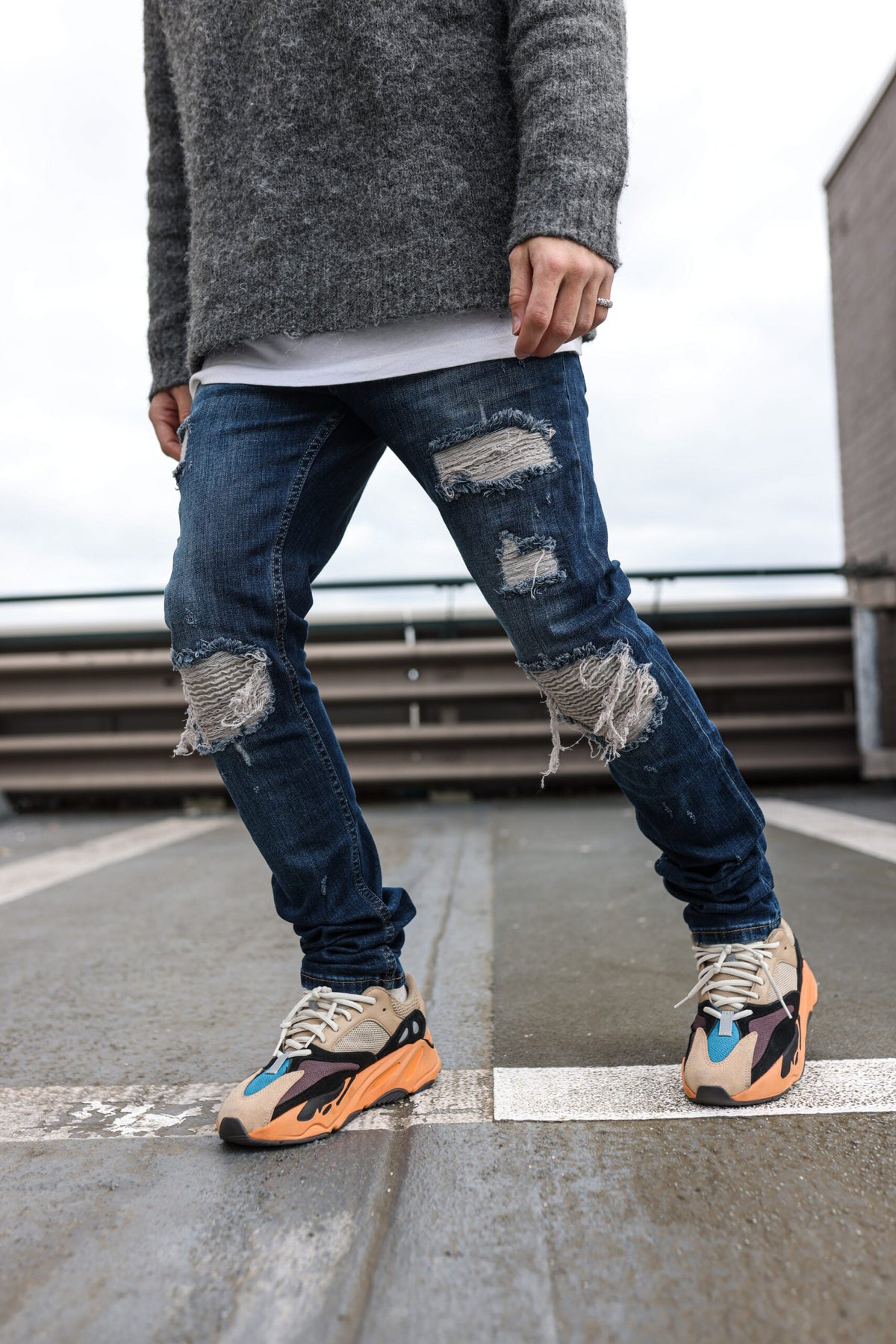 Model in de Force Dark Blue Jeans met scheuren en sneakers op een dak in de stad